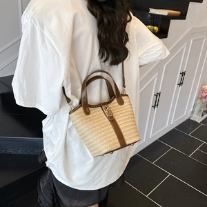 Fashionable woven straw bucket bag with brown leather trim shown as a crossbody
