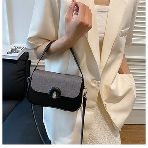 Détail d'un sac à main noir et gris avec fermoir métallique sur un costume blanc