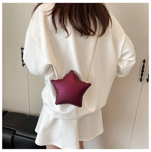 Star-shaped burgundy acrylic box bag with golden chain strap on a model's shoulder