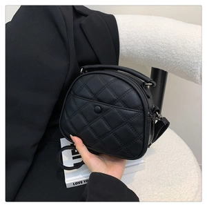 Close-up of black quilted leather shoulder bag with top handle on a white textured chair