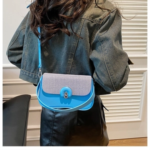 Sac bandoulière bleu ciel avec rabat texturé et fermoir circulaire porté par un mannequin