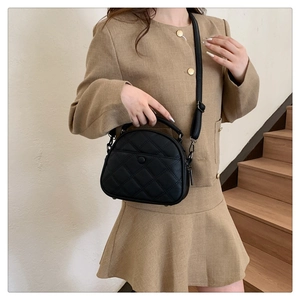 Detail of black quilted crossbody bag with top handle and front pocket shown on a model