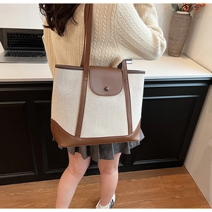 Détail d'un grand sac fourre-tout en toile avec finitions en cuir marron porté par un mannequin