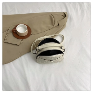 Detail view of cream quilted crossbody bag featuring dual zippers and black fabric lining