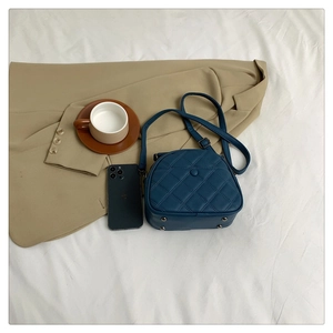 Flat lay of navy blue quilted crossbody bag with metal feet and adjustable strap detail
