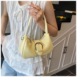 Detailed view of glossy cream underarm bag with oversized silver buckle on a model