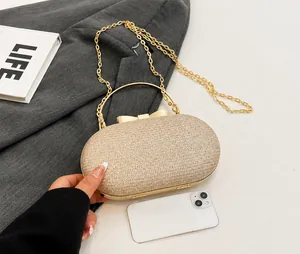 Detail of glitter gold evening bag with round handle and bow clasp next to a phone
