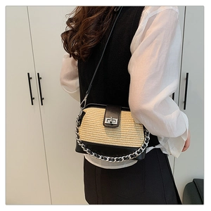 Detail of contrast stitch straw handbag with black leather trim and metal lock closure