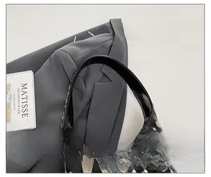 Close-up of black patent leather handbag featuring silver metal rivets and sturdy handle