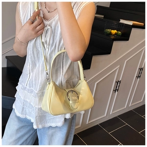 Detail of a creamy yellow glossy leather underarm bag with a silver round buckle