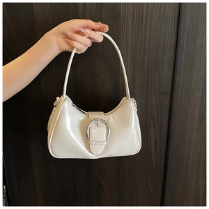 Detail of white glossy patent leather bag featuring a bold silver circular metal buckle