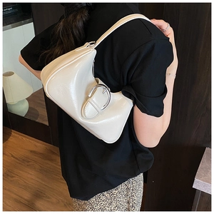 Detail of cream glossy underarm bag with silver horseshoe buckle on model with black outfit