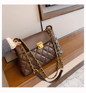 Detail der dunkelbraunen Stepptasche aus Leder mit Goldkette auf einem Holztisch