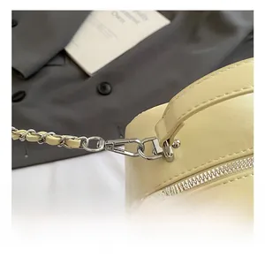 Detail of silver metal hook and woven chain strap on quilted beige crossbody bag
