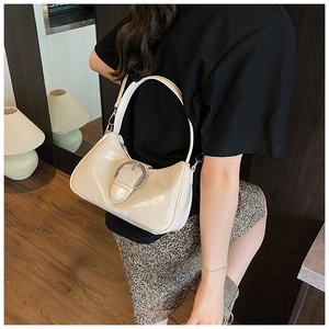 Detail of cream patent leather underarm bag featuring a large silver oval metal buckle