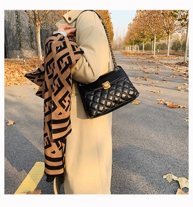 Nahaufnahme der schwarzen gesteppten Ledertasche mit Goldkette und Logo-Musterschal