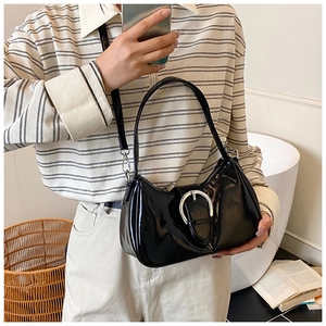 Detail of glossy black leather shoulder bag featuring a prominent silver round buckle