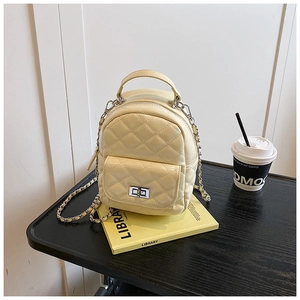 Detailed close-up of a pale yellow quilted mini backpack on a black wooden desk