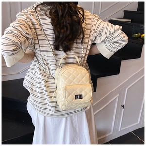 Rear view of a model wearing a beige quilted mini backpack with woven chain straps