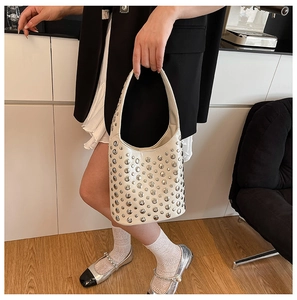 Detail of beige hobo bag featuring silver rivets and matte leather held by a model