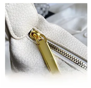 Close-up of smooth gold zipper on white lychee textured crossbody handbag detail