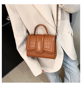 Borsa a tracolla marrone con motivo coccodrillo e catena indossata con un abito bianco