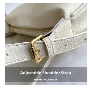 Detail of adjustable leather shoulder strap with gold buckle on a beige pebble grain bag