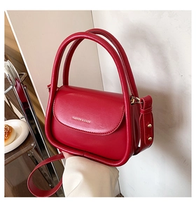 Close-up of red matte leather handbag with gold lettering and adjustable shoulder strap