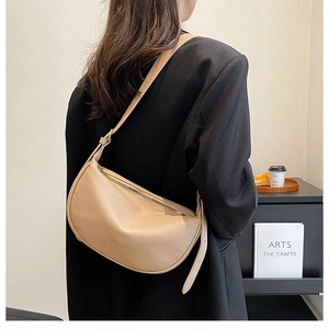 Close-up of beige grained leather crescent bag worn by a model in a minimal office setting