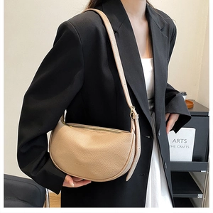 Detail of beige crescent shoulder bag with lychee texture and slim strap over a black suit