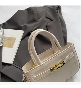 Detail of cream faux crocodile texture handbag with gold twist lock on grey blazer
