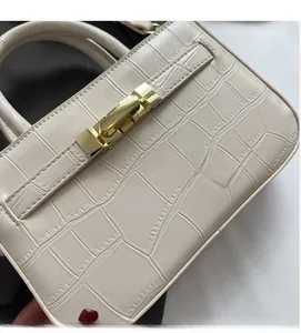 Detail of creamy white faux crocodile leather texture and golden metal lock on handbag
