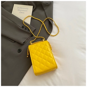 Macro detail of yellow quilted crossbody bag featuring a gold metal chain strap