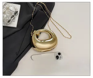 Dettaglio della borsa clutch tonda in metallo dorato con catena e finitura lucida