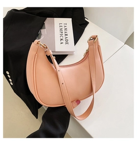 Detail of peach pink crescent moon shoulder bag with gold hardware on a desk