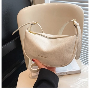 Detail of cream crescent bag featuring lychee grain leather and adjustable strap