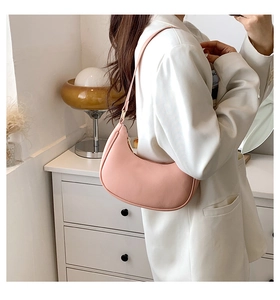 Side view of a light pink half-moon hobo bag worn by a model in a minimalist room