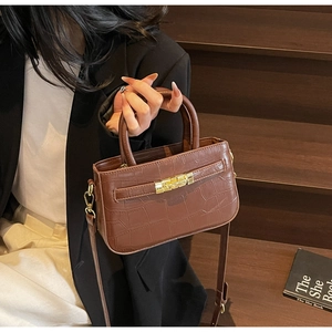 Detail of a dark brown crocodile pattern handbag with gold clasp and leather strap