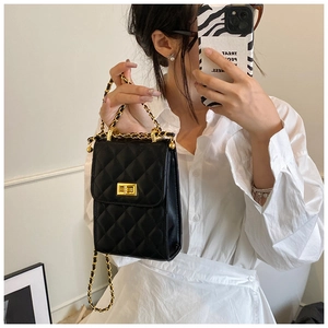 Detail of black quilted chain bag with gold metal twist lock and leather strap