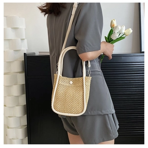 Detail of woven straw bucket bag with white leather trim and adjustable shoulder strap