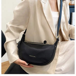 Detail of black crescent leather crossbody bag worn over a beige blazer for city style