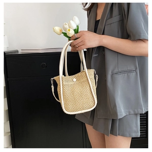 Detail of woven straw bucket bag with white leather trim and round buckle on a gray suit