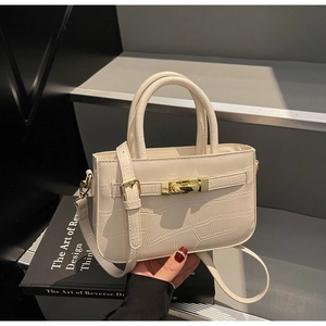 Detailed view of cream crocodile-embossed leather handbag with gold metal clasp