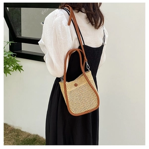 Outdoor model shot showing the side view of a round woven straw shoulder bag with brown straps