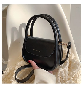 Detail of matte black saddle bag with gold metal hardware and detachable strap