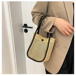 Detail of woven straw tote bag with brown leather trim and circular decorative buckle