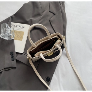 Top view of cream textured leather handbag with interior zipper layer on grey blazer