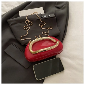 Detailed top view of red patent leather clutch with gold handle and snake chain on suit