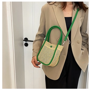 Detail of woven straw bucket bag with green leather trim and strap on a beige suit model