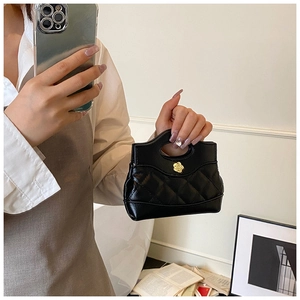 Close-up of quilted black mini bag with gold flower buckle and oval handle detail